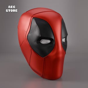 Può includere: Una maschera di Deadpool rossa e nera con finitura metallica. La maschera presenta copriocchi neri con una trama a rete ed è ambientata su uno sfondo grigio. Il testo "AEG STORE" è visibile nell'angolo in alto a sinistra.