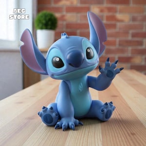 May include: A blue Stitch figurine with large ears, sitting on a wooden surface. The figurine has a light blue belly and dark blue claws. The figurine is waving with its right hand. The text "AEG STORE" is in the upper left corner.