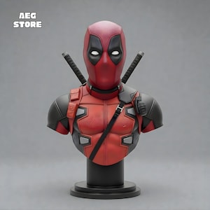 Può includere: Busto del personaggio Deadpool, con maschera rossa e nera dettagliata, armatura sulle spalle e due spade katana. La base è nera. Il testo "AEG STORE" è visibile in alto a sinistra.