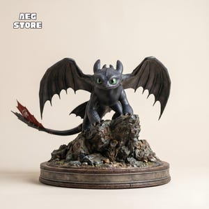 Könnte beinhalten: Eine schwarze Drachenstatue mit ausgebreiteten Flügeln und leuchtend grünen Augen, die auf einem detaillierten Felsensockel sitzt. Der Drachenschwanz hat rote Akzente. Die Basis ist rund und trägt den Text "AEG STORE".