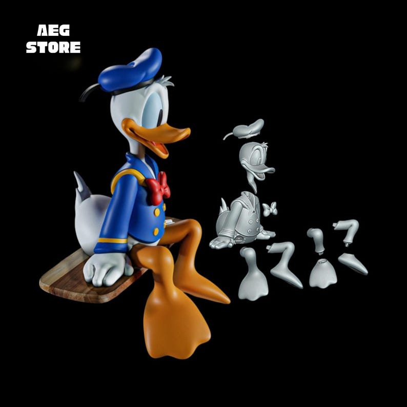 May include: A Donald Duck figurine with a blue sailor suit, hat, and red bow tie, sitting on a wooden plank. The image includes the text "AEG STORE" in the upper left corner, and several disassembled parts of the figurine.