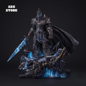 May include: A detailed figurine of a dark armoured warrior wearing a horned helmet and a flowing black cape. The figure holds a glowing blue sword and stands on a rocky base decorated with skulls, chains, and blue crystals. Text reads AEG STORE.