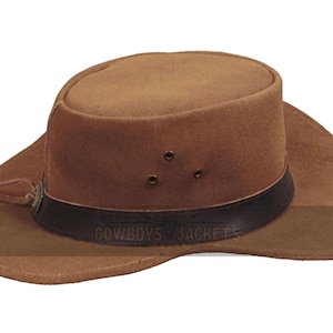 May include: A brown cowboy hat with a wide brim and a dark band. The hat has three small air vents and a leather strap with a decorative element. The text "COWBOYS JACKETS" is printed on the band.