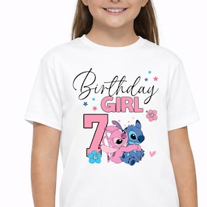 May include: White t-shirt with the text "Birthday Girl 7" in black and pink script. The number 7 is pink, and the shirt features cartoon characters hugging, with blue and pink accents.