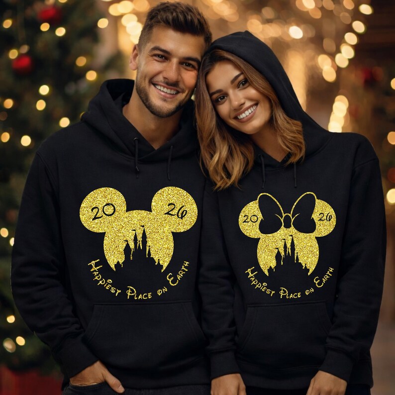 K&ouml;nnte beinhalten: Schwarze Kapuzenpullover mit goldenen Glitzer-Mickey-Mouse- und Minnie-Mouse-Designs. Die Sweatshirts zeigen die Zahlen "2026" und den Text "Happiest Place on Earth".
