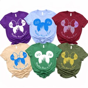 K&ouml;nnte beinhalten: Sechs kurz&auml;rmelige T-Shirts in verschiedenen Farben, jeweils mit einem Mickey Mouse-Silhouetten-Design. Das Design enth&auml;lt die Zahlen "20" und "26", eine Schleife, ein Schloss und den Text "Happiest Place on Earth".