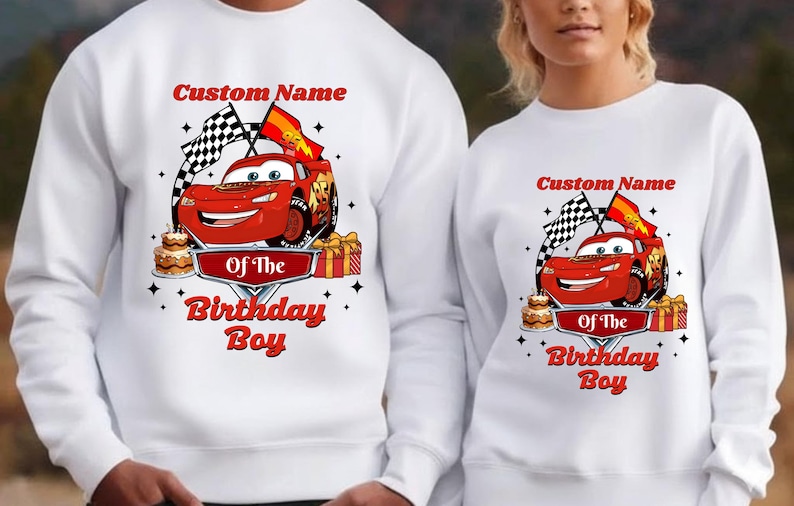 May include: White sweatshirt featuring a red race car graphic with the text "Custom Name Of The Birthday Boy". The design includes checkered flags, a birthday cake, and gift boxes. The sweatshirt is suitable for a birthday celebration.