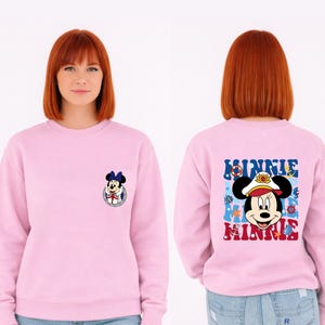 May include: A light pink sweatshirt featuring Minnie Mouse. The front has a small Minnie Mouse graphic. The back has a larger graphic of Minnie Mouse in a sailor hat with the word "MINNIE" in blue and red.