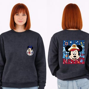 May include: Navy blue sweatshirt featuring Minnie Mouse in a sailor outfit. The front has a small Minnie Mouse graphic, while the back displays a larger design with the words "Minnie Mouse" and nautical elements like anchors and seashells.