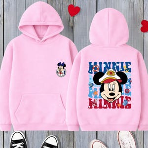 May include: Pink hooded sweatshirt featuring a Minnie Mouse graphic on the front and back. The front has a small Minnie Mouse emblem, while the back displays a larger Minnie Mouse design with the name "Minnie".
