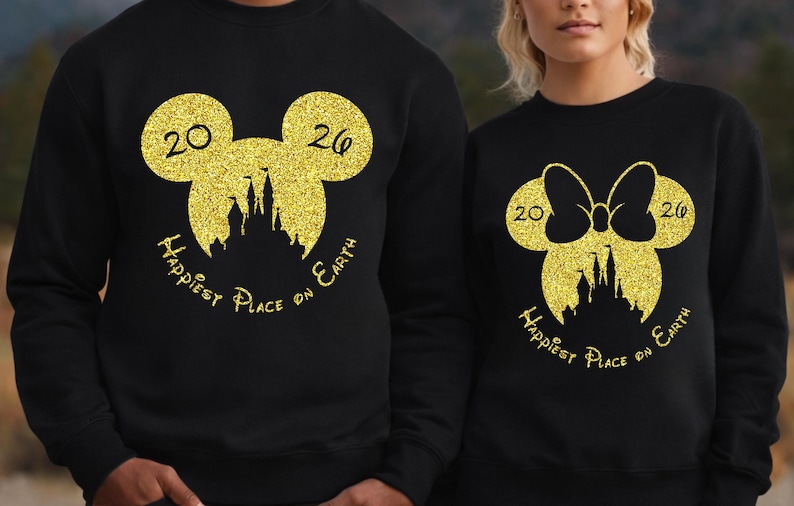 K&ouml;nnte beinhalten: Schwarze Sweatshirts mit goldglitzernden Mickey Mouse- und Minnie Mouse-Designs. Das Mickey Mouse-Design hat die Zahlen "20" und "26" und die Worte "Happiest Place on Earth". Das Minnie Mouse-Design hat eine Schleife.