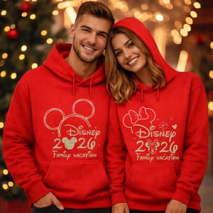 May include: Two red hoodies with the Disney logo and the text "Disney 2026 Family Vacation." One hoodie features Mickey Mouse ears, the other Minnie Mouse ears. Both have a front pocket and a drawstring hood.