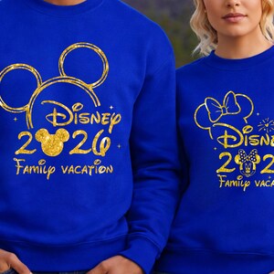 May include: Two blue sweatshirts with gold glitter designs. One features Mickey Mouse ears and the text "Disney 2020 Family Vacation." The other has Minnie Mouse ears and the same text. A fun matching set for a family vacation.