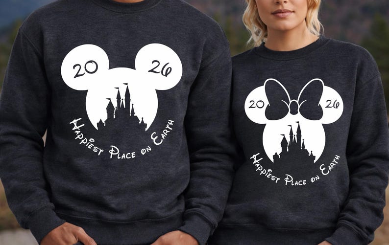K&ouml;nnte beinhalten: Zwei dunkelgraue Sweatshirts mit wei&szlig;en Grafikdesigns. Eines zeigt einen Mickey Mouse-Kopf mit den Zahlen "20" und "26", eine Schlosssilhouette und den Text "Happiest Place on Earth". Das andere hat einen Minnie Mouse-Kopf mit einer Schleife.