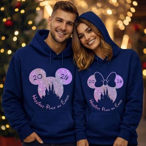 K&ouml;nnte beinhalten: Marineblaue Kapuzenpullover mit Mickey Mouse und Minnie Mouse Design. Das Design beinhaltet die Zahlen "20" und "26", eine Schlosssilhouette und den Text "Happiest Place on Earth". Die Sweatshirts haben eine Vordertasche.