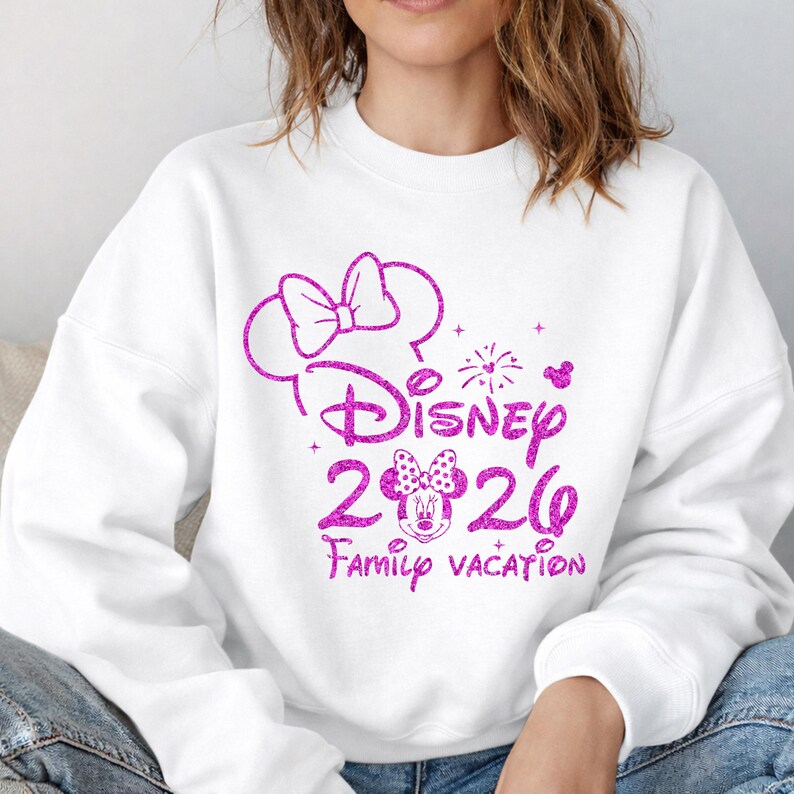 May include: White sweatshirt with a pink glitter design featuring the word "Disney" above the numbers "2026" and the words "Family Vacation". The design includes Mickey Mouse ears, a bow, and a Minnie Mouse face.