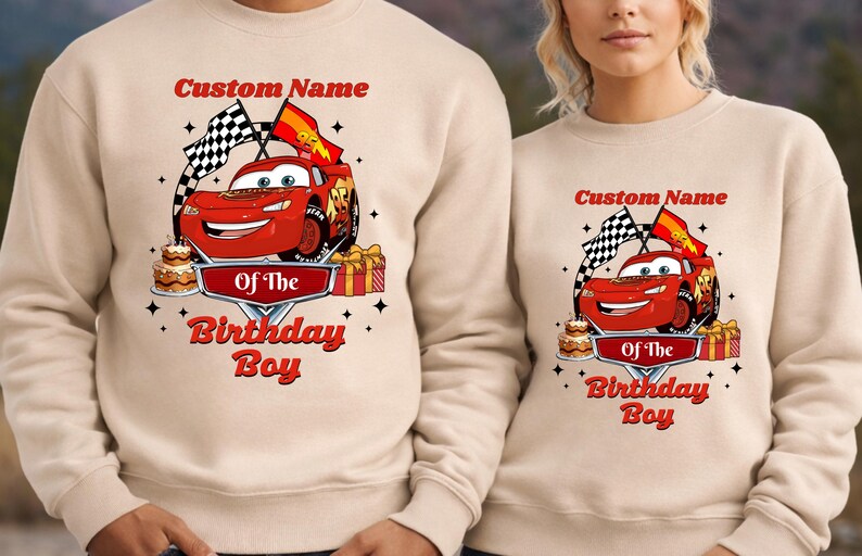 May include: Beige sweatshirt featuring a red cartoon race car with the text "Custom Name" above and "Of The Birthday Boy" below. The design includes checkered flags, a cake, and wrapped gifts.