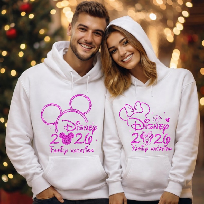 May include: Two white hooded sweatshirts with pink glitter Disney graphics. One features Mickey Mouse ears, the other Minnie Mouse ears. Both say "Disney 2026 Family Vacation."