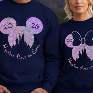 K&ouml;nnte beinhalten: Marineblaue Sweatshirts mit glitzernden Mickey Mouse und Minnie Mouse Kopf-Designs. Jedes Design enth&auml;lt die Zahlen "20" und "26", eine Schloss-Silhouette und den Text "Happiest Place on Earth" in rosa Schrift.