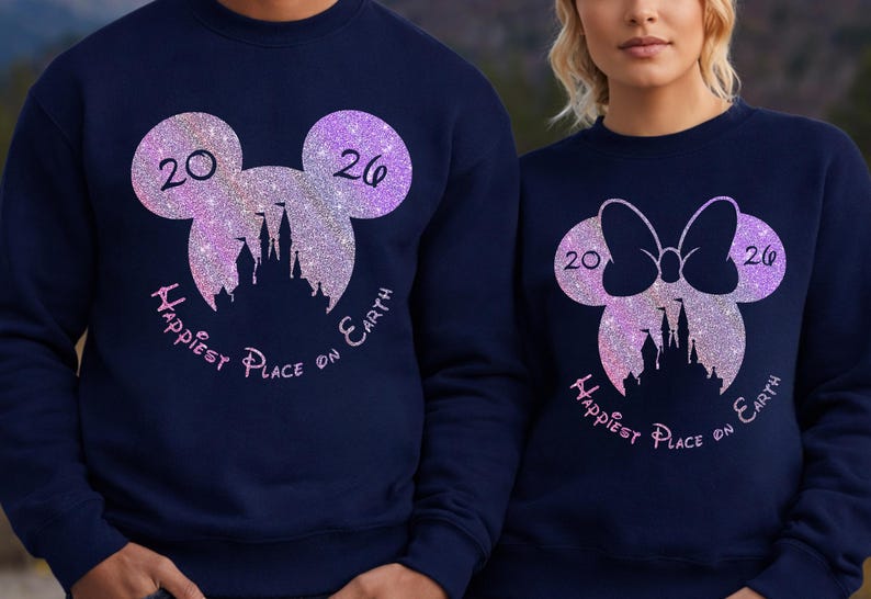 K&ouml;nnte beinhalten: Marineblaue Sweatshirts mit glitzernden Mickey Mouse und Minnie Mouse Kopf-Designs. Jedes Design enth&auml;lt die Zahlen "20" und "26", eine Schloss-Silhouette und den Text "Happiest Place on Earth" in rosa Schrift.