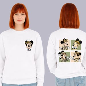 May include: White sweatshirt with Minnie Mouse design. The front has a small Minnie Mouse graphic with a bow and the word "Minnie". The back features four square images of Minnie Mouse in safari outfits. A comfortable, casual top.