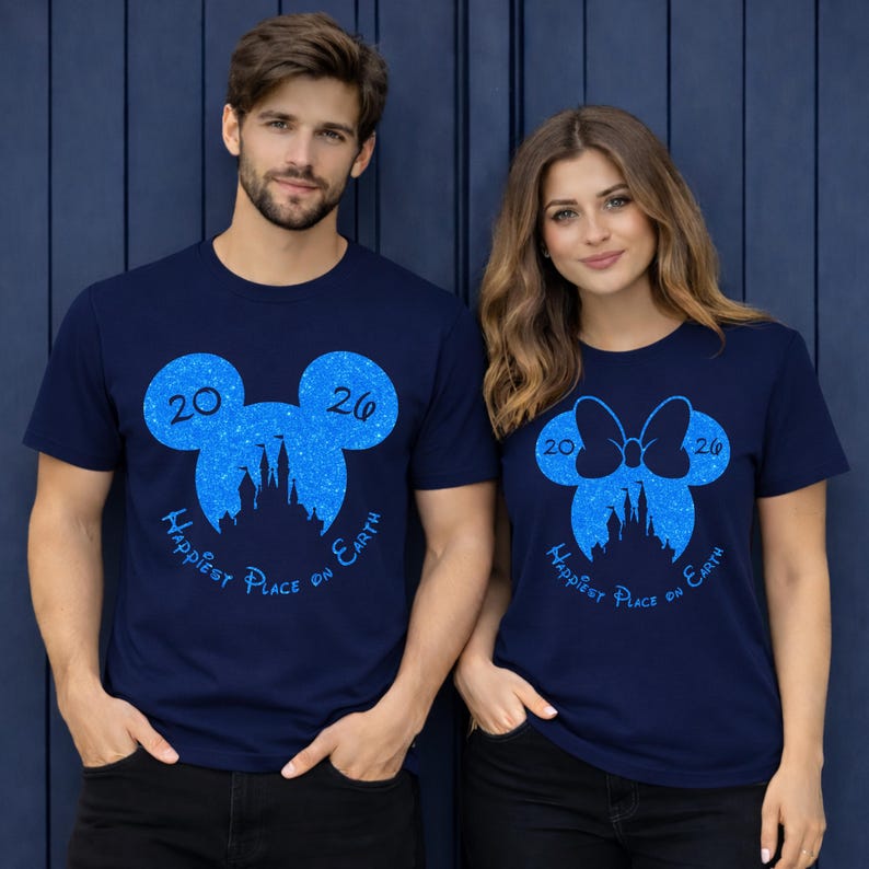 K&ouml;nnte beinhalten: Marineblaue T-Shirts mit einem blauen Glitzerdesign von Mickey Mouse-Ohren und einer Schleife, mit dem Text "2026 Happiest Place on Earth". Ein Mann und eine Frau tragen diese T-Shirts.