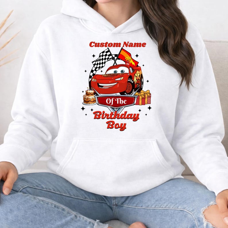 May include: White hoodie with a graphic of a red race car, checkered flags, and the text "Custom Name Of The Birthday Boy". The design includes a cake and wrapped gifts.