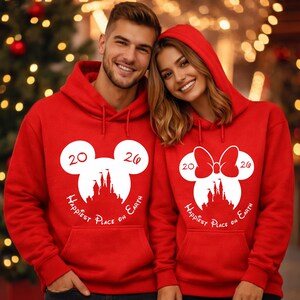 K&ouml;nnte beinhalten: Rote Kapuzenpullover mit wei&szlig;en Grafikdesigns. Ein Kapuzenpullover zeigt einen Mickey Mouse-Kopf mit den Zahlen "20" und "26" und dem Text "Happiest Place on Earth". Der andere Hoodie hat ein Minnie Mouse-Schleifendesign mit demselben Text und denselben Zahlen.
