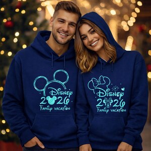 May include: Two navy blue hooded sweatshirts with a Disney theme. One features Mickey Mouse ears, the other a Minnie Mouse bow. Both have "Disney 2020 Family Vacation" in teal. The sweatshirts have a front pocket and drawstrings.