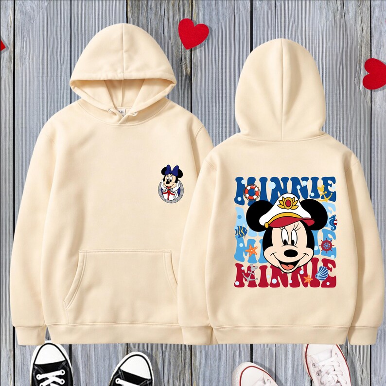 May include: Cream-colored hoodie with a front pocket and a hood. The front features a small Minnie Mouse graphic, while the back displays a larger Minnie Mouse design with the name "MINNIE" in blue and red lettering.