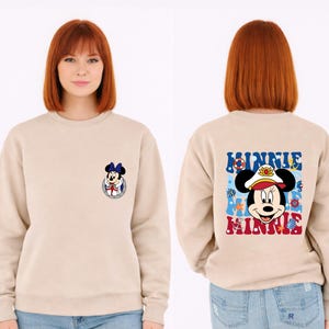 May include: Beige sweatshirt featuring a Minnie Mouse graphic on the front and back. The front graphic is a small Minnie Mouse in a sailor outfit. The back graphic says "Minnie" with a nautical theme, including a sailor hat and anchor.