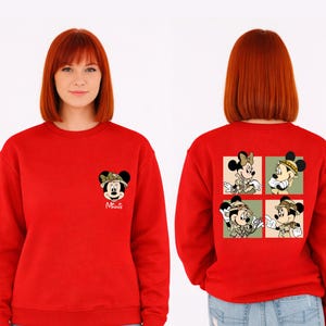 May include: A bright red sweatshirt with Minnie Mouse safari designs. The front has a small Minnie Mouse graphic with the name "Minnie". The back features a four-panel design of Minnie in various safari poses.
