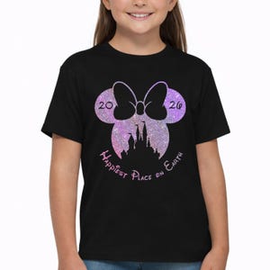K&ouml;nnte beinhalten: Schwarzes T-Shirt mit einem Minnie-Mouse-Design, einschlie&szlig;lich einer Schleife, den Zahlen "20" und "26" sowie einer Schloss-Silhouette. Der Text "Happiest Place on Earth" ist ebenfalls enthalten.