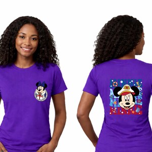 May include: Purple t-shirt featuring Minnie Mouse. The front has a small graphic of Minnie Mouse in a blue bow. The back has a larger graphic of Minnie Mouse in a sailor hat with nautical elements. The shirt is short-sleeved.
