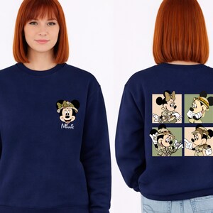 May include: A navy blue sweatshirt with Minnie Mouse in safari gear. The front has a small Minnie graphic with the name "Minnie" in white. The back features a four-panel design of Minnie and Mickey in safari outfits.