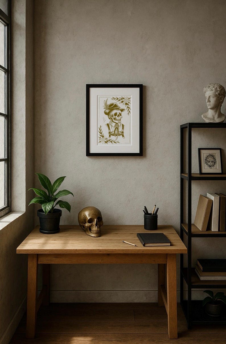 Puede incluir: Una impresi&oacute;n enmarcada de un esqueleto con sombrero y chaleco cuelga sobre un escritorio de madera. Una calavera de bronce, una planta en maceta y un cuaderno negro est&aacute;n sobre el escritorio. Una estanter&iacute;a de metal negro con libros y un busto es visible.