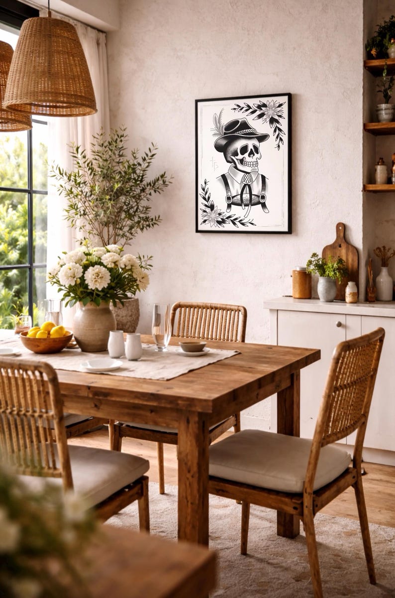 Puede incluir: Un comedor con mesa y sillas de madera, una impresi&oacute;n en blanco y negro enmarcada de un esqueleto con vestimenta tradicional y un jarr&oacute;n con flores blancas. La habitaci&oacute;n tiene una paleta de colores neutros.