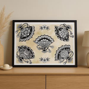 Op de afbeelding: Zwart ingelijste kunstdruk met vijf gedetailleerde ventilatorillustraties met bloemmotieven. De ventilatoren zijn in zwart en wit, tegen een beige achtergrond. Het kunstwerk wordt op een houten oppervlak weergegeven.