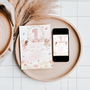 May include: A pink and floral fairy-themed invitation and a smartphone displaying the same design, both on a round tray. The invitation reads "Amelia's fairy first birthday" with fairy illustrations and the number 1.