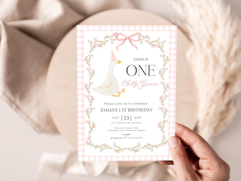 Op de afbeelding: Een roze en witte geruite verjaardagsuitnodiging met bloemen- en strikaccenten. De uitnodiging toont een cartoon gans met een feesthoedje en de tekst "EMMA IS ONE Silly Goose". De uitnodiging is voor Emma's 1e verjaardag.