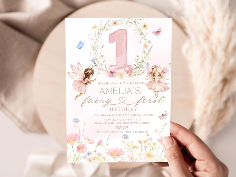 May include: A whimsical invitation for Amelia's first birthday, featuring a pink number one, floral accents, and fairy illustrations. The text reads "Amelia's fairy first birthday" with event details. The invitation is held by a hand.