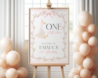Puede incluir: Un letrero enmarcado sobre un caballete con una ilustración de un ganso, el texto "ONE Silly Goose" y "Bienvenida al 1er Cumpleaños de Emma". Globos color melocotón están agrupados a ambos lados del letrero. El letrero tiene un borde floral rosa.