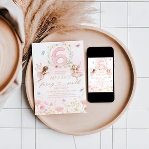 May include: A pink and floral birthday invitation with the number 6, fairies, and the text "Amelia's fairy sixth birthday" is displayed on a wooden tray next to a smartphone with the same design. Dried flowers and a wooden bowl are also in the image.