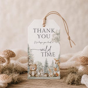 May include: A rectangular white paper gift tag with a tan string loop, featuring the printed text "THANK YOU We hope you had a wild TIME" and watercolour illustrations of a bear, owl, hedgehog, rabbit, deer, and fox in a forest setting.