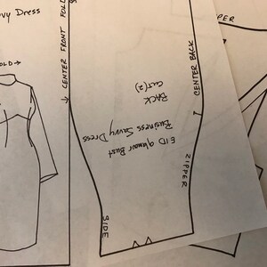 May include: A collection of dress patterns labeled "Business Savvy Dress" and "EID glamour Bust". The patterns are drawn in black ink on white paper, with annotations for cutting and assembly. The dress design includes long sleeves and a fitted bodice.