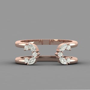 May include: Rose gold double-band ring with a cluster of marquise and round-cut diamonds. The diamonds are arranged in a curved pattern on each band, creating a unique and elegant design. The ring is set against a gray background.