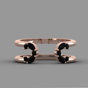 May include: Rose gold double-band ring with black gemstone accents. The ring features two parallel bands connected by curved sections, each adorned with clusters of black gemstones. The design is symmetrical and modern, set against a neutral background.
