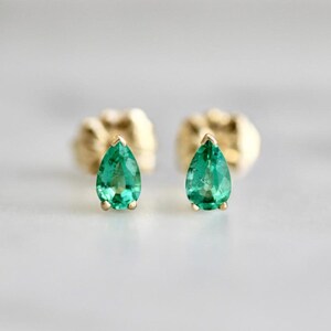 May include: A pair of stud earrings featuring pear-shaped green gemstones set in yellow gold. Each earring showcases a faceted teardrop-cut green stone secured by a gold prong setting, with the gold post and backing visible behind the main stone.