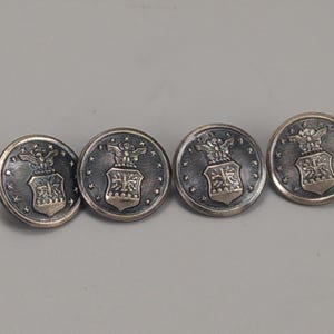 Puede incluir: Una taza de cerámica blanca con un asa negra y el texto "But First, Coffee" en negrita negra. La taza se encuentra sobre un fondo borroso, sugiriendo un ambiente acogedor.