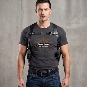 May include: A black leather shoulder holster system worn over a dark gray t-shirt featuring the text Leather Nirvana HandCrafted Goodness in a decorative gold frame. The holster includes two side pouches and adjustable straps with metal buckles.